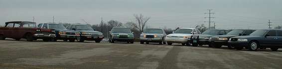 Front view of a line of police cars, including a 1998 Ford Crown Victoria