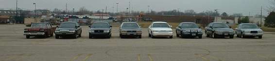 Several sedans parked in a lot, including a dark Crown Victoria and a silver Crown Victoria