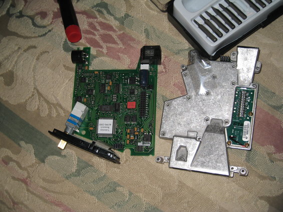 Electronic circuit board with components and a metal casing, along with a screwdriver and a set of precision screwdrivers