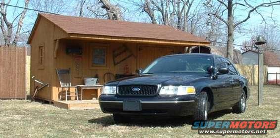 Black 1998 Ford Crown Victoria parked in front of a wooden shed