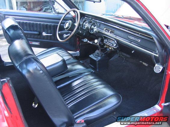 Red car interior with black vinyl seats, wood-rimmed steering wheel, and dashboard with 'COUGAR' badging