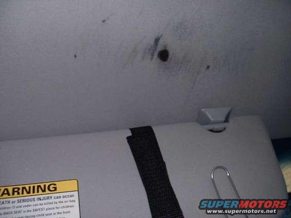 Car ceiling with some dark marks and a sun visor. Warning label visible on visor