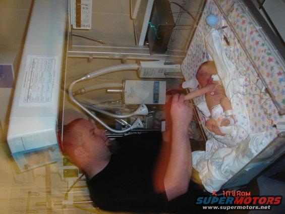 Father looking at his newborn baby in an incubator in a hospital room
