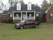 2005 Ford F-150 - A maroon Ford F-150 pickup truck is parked on the lawn in front of a large brick house with a white porch.
