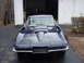1964 Chevrolet Corvette - A dark blue Chevrolet Corvette is parked in front of a garage, showing its distinctive front end and hood scoop.