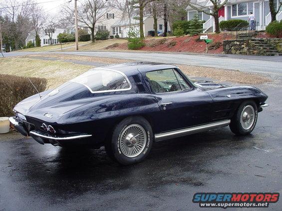 Dark blue coupe parked on wet asphalt, houses in background