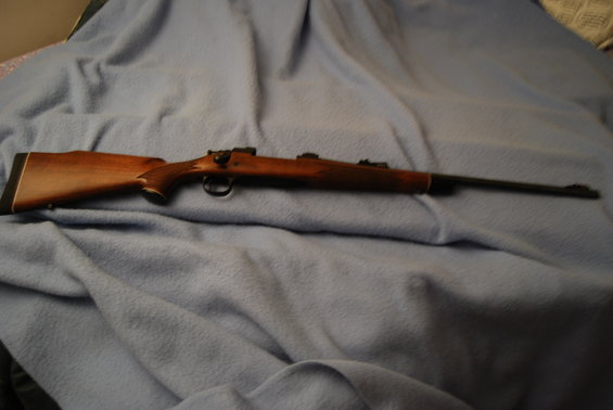 Wooden rifle with a blued barrel and bolt action, resting on a blue blanket