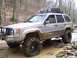 2002 Ford Sport Trac - A muddy Jeep Grand Cherokee navigates a water-filled trail in a wooded area.