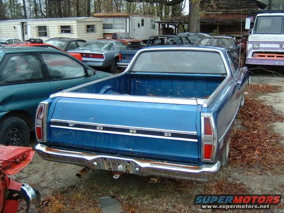 Rear view of a blue Ford Ranchero pickup truck, parked outdoors with other vehicles and trailers