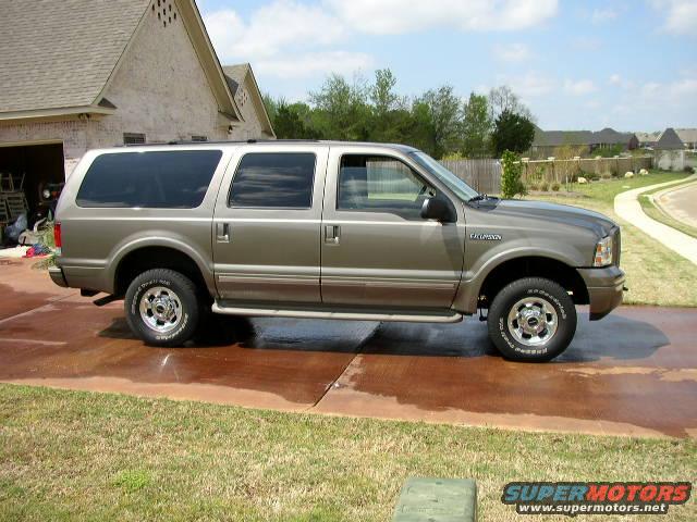 Side view of a tan Ford Excursion parked on a driveway. It has tinted windows and chrome wheels
