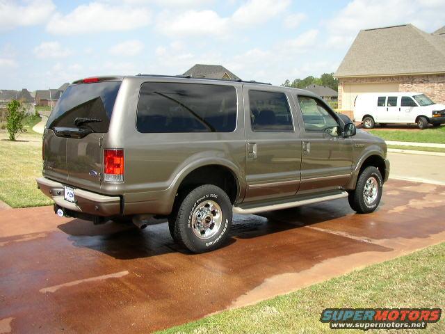 Brown Ford Excursion parked on a wet driveway, side view. A white van is in the background