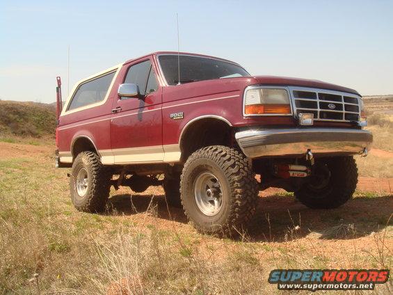 Red 1992 Ford Bronco with off-road tires and white top parked on a grassy hill