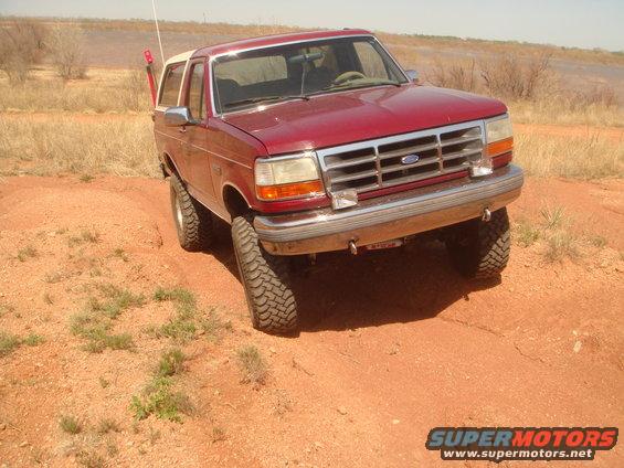 Red 1992 Ford Bronco on a dirt trail with a white top