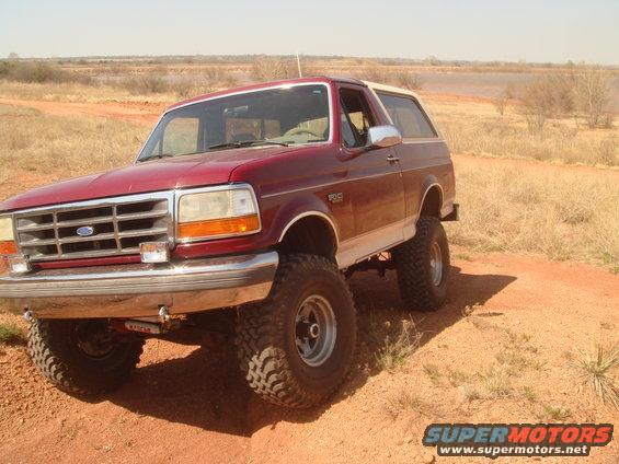 Maroon Ford Bronco with white top and lifted suspension on dirt road