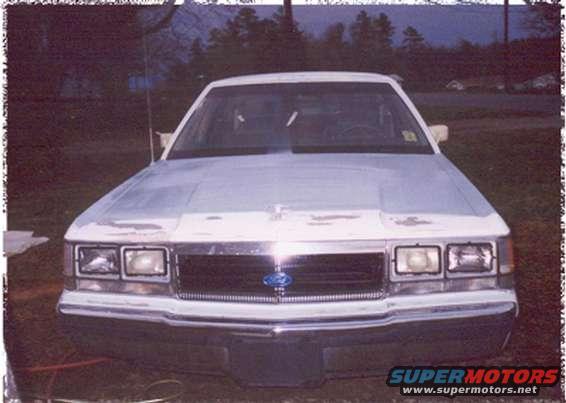 White sedan front view, showing a chrome grille with a blue Ford emblem. The paint is peeling on the hood