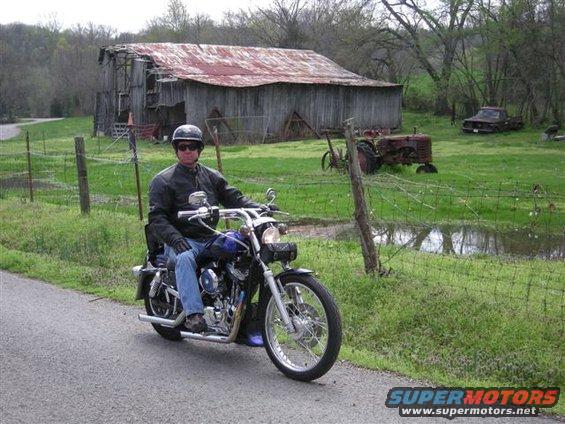 Blue motorcycle with rider on a rural road near a barn