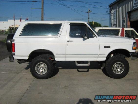 White Ford Bronco, lifted, side view. Another vehicle partially visible behind it