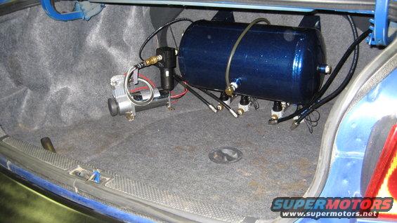 Blue air suspension tank and silver compressor mounted in a car's carpeted trunk