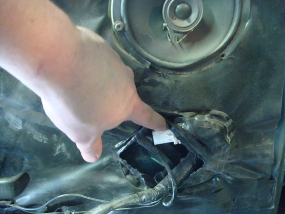 Door panel with speaker cutout and exposed wiring, a hand points to a connector