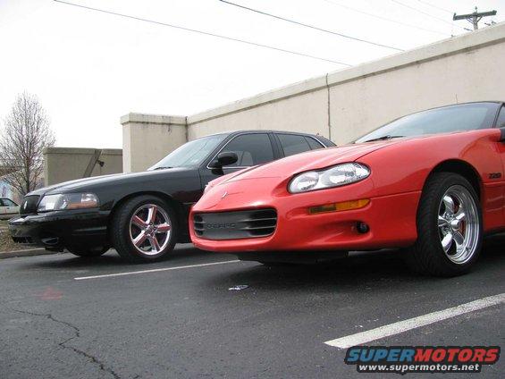 Black sedan parked next to a red sports car, front 3/4 view