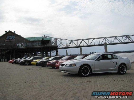 Silver Ford Mustang coupe with black wheels parked in a line with other Mustangs
