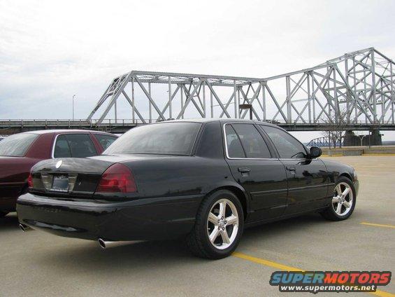 Black sedan parked near a bridge, another car is partially visible on the left