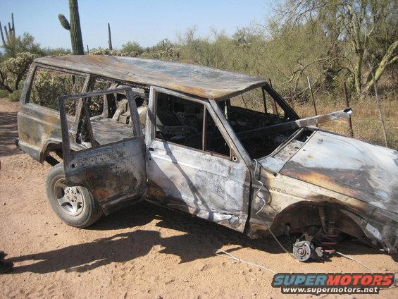 Burnt SUV with doors open, missing front passenger wheel, in a desert landscape