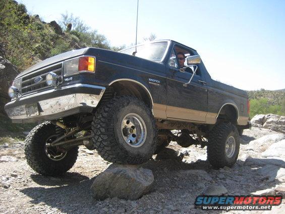 Black and tan lifted 1991 Ford Bronco off-roading on rocks