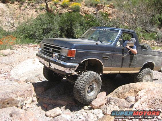 Dark blue Ford Bronco with lifted suspension and large tires navigating rocky terrain