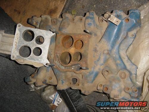 Blue engine intake manifold with a carburetor mounting plate, showing rust and dirt