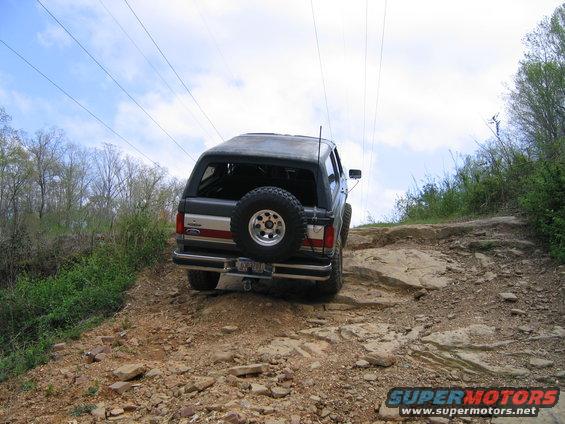 Bronco driving up rocky trail, spare tire on back