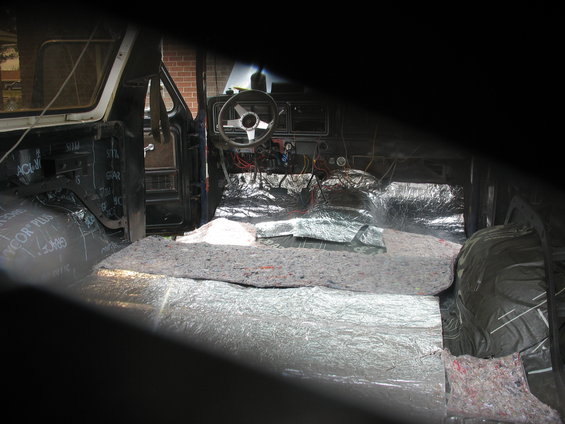 Vehicle interior with sound deadening material on floor and doors. Steering wheel and dashboard visible