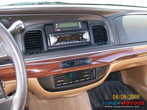 Car dashboard with aftermarket JVC stereo, digital clock, and climate controls. Wood trim accents the dash