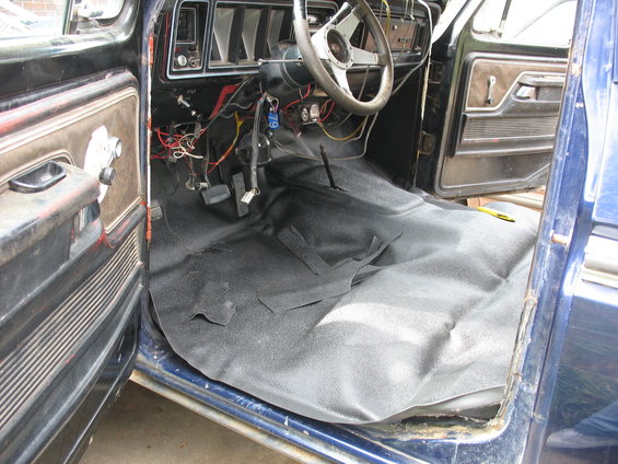 1978 Ford Bronco interior with new black carpet partially installed, exposed wiring, and worn door panels