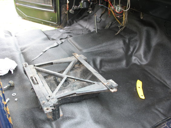 Interior floor of a vehicle with black textured matting, a removed seat bracket, and exposed wiring under the dashboard