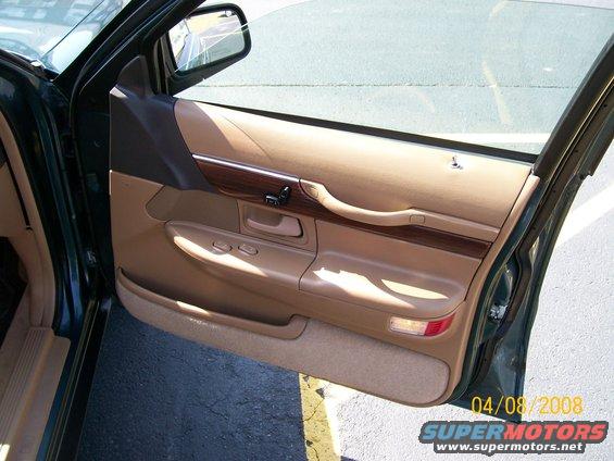 Car door panel with tan upholstery, wood trim, and window controls
