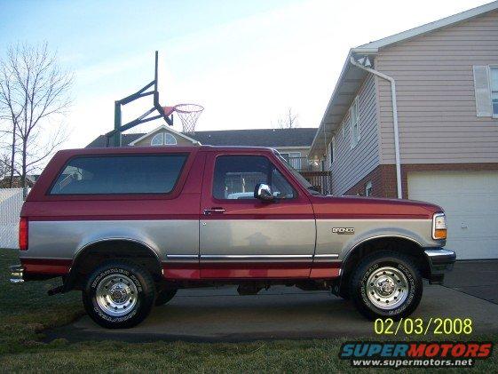 Side view of a red and silver 1994 Ford Bronco parked in a driveway