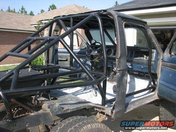 Roll cage inside a dark blue SUV, viewed from the passenger side. The interior is stripped down