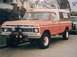 1977 Ford F-150 - Orange 1977 Ford F-150 pickup truck equipped with a camper shell and a winch on the front bumper.