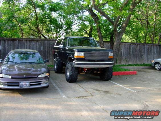 Black 1992 Ford Bronco with lifted suspension and large tires parked next to a dark sedan