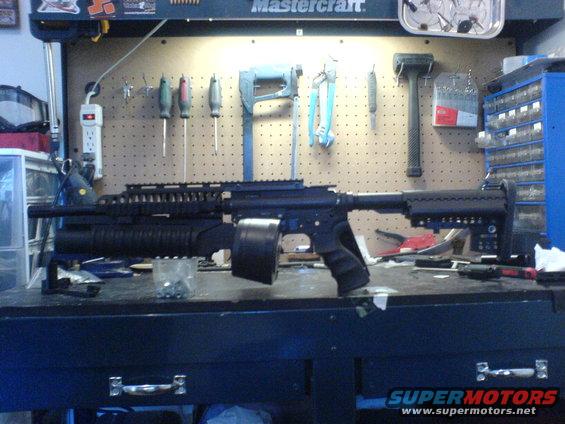 Assault rifle with drum magazine on a workbench with tools