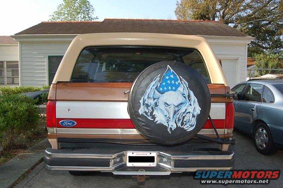 1989 Ford Bronco rear bumper, taillights, and spare tire cover with eagle graphic. Another car is parked to the right