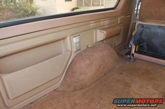 1989 Ford Bronco interior showing tan door panel with map pocket and rear wheel well covered in brown carpet