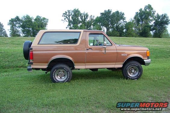 Brown 1987 Ford Bronco parked on grass, side view, spare tire on rear door