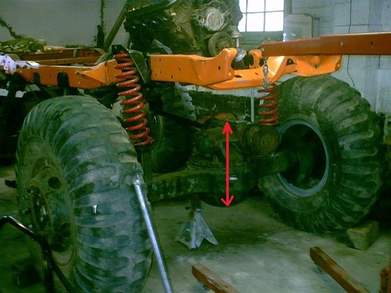 Vehicle chassis on jack stands with large off-road tires and suspension components visible