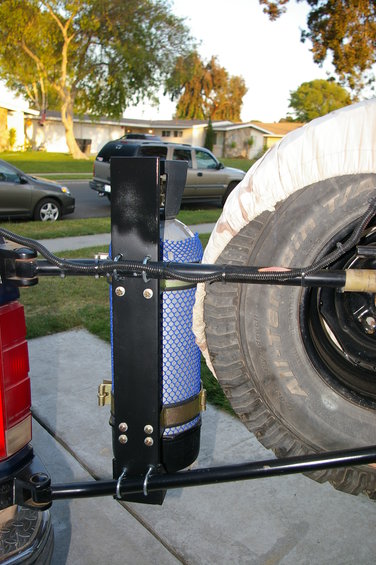 Spare tire carrier mounted on a vehicle's rear, holding a propane tank
