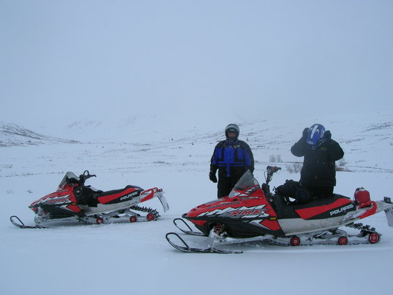 two red and white snowmobiles parked in snow with two people wearing helmets and winter gear