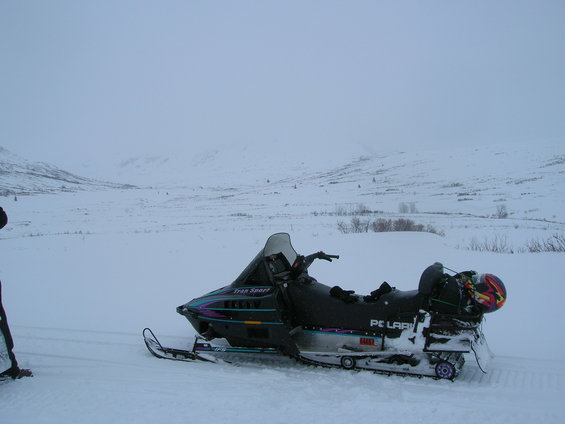 Black Polaris snowmobile with purple and teal graphics, parked in snow with a helmet on the back