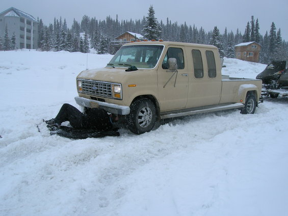 Tan extended cab pickup truck with a person underneath, stuck in snow