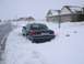 1999 Ford Crown Victoria - A dark blue sedan is partially buried in snow on the side of a street in front of houses.
